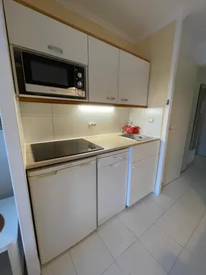 a small kitchen with white cabinets and a microwave at Appartement Cannes, Piscine - Terrasse, Jardin Privatif - 4 Personnes in Cannes