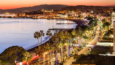 a city with palm trees and the ocean at night at Suite Palais des Festivals & Croisette 1 min in Cannes