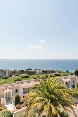 a palm tree in front of a building and the ocean at Résidence Cannes Villa Francia - maeva Home - Appartement design 2 pièces 3 personnes avec vue mer - Prestige - Super Home MAE-4317 in Cannes